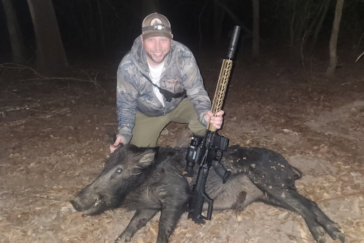 Hunter with three hogs and a thermal-equipped rifle after a night hunt